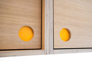 Close-up of yellow plywood door fronts with circular finger pull detail
